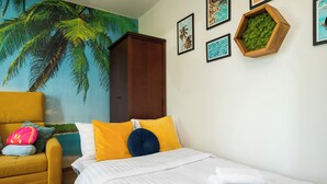A bedroom with a bed, a yellow armchair, a mural of palm trees, and framed pictures on the wall. - Ziemowita Colorful Studio (Warszawa)