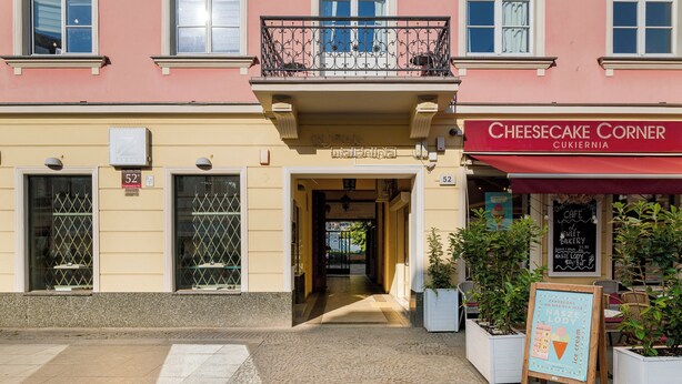 A building with a red awning labeled 'Cheesecake Corner' and a signboard with a heart and ice cream symbol. - Nowy Świat Sunny Side Apartment (Warszawa)