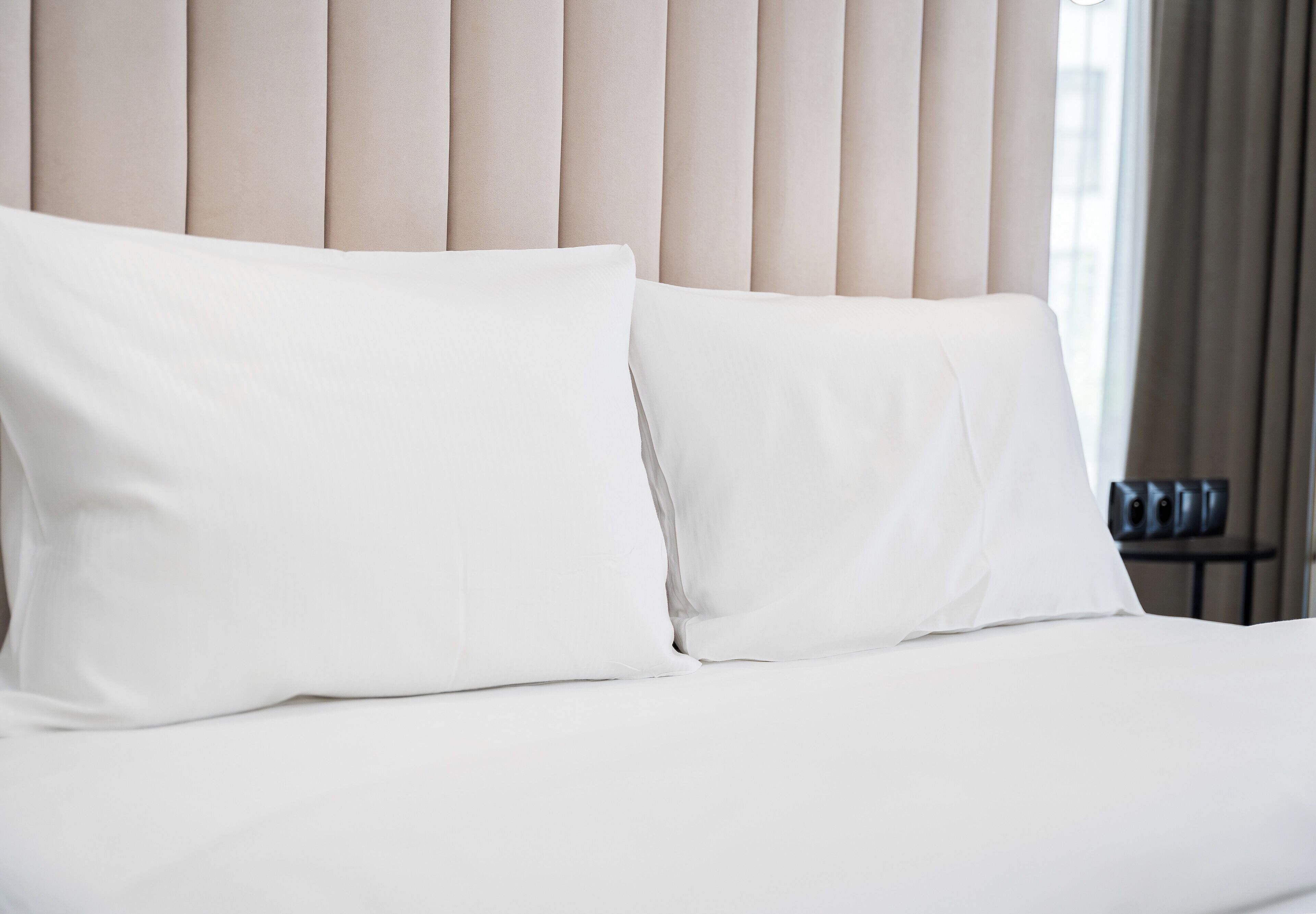 Una cama con ropa de cama blanca y cabecera de listones verticales.