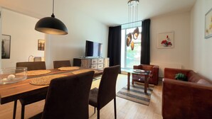 Ett modernt vardagsrum med en matplats, en platt-TV och ett stort fönster med gardiner.