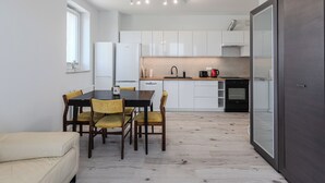 A modern kitchen with white cabinets, a dining table with chairs, a refrigerator, and a coffee maker.