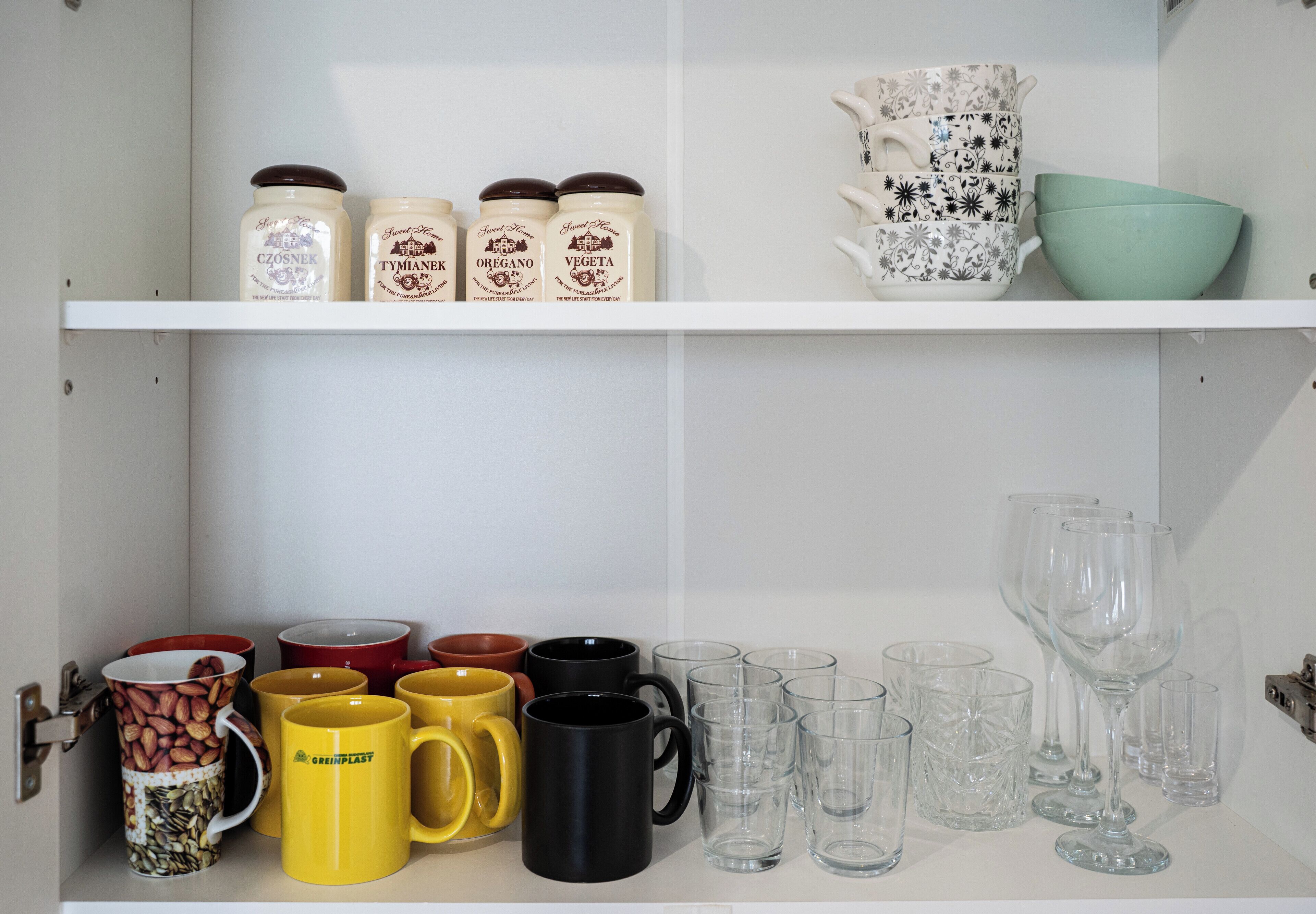 A kitchen shelf with jars, mugs, and glassware.