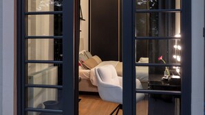 Ein Zimmer mit einem Bett, einem Sessel, einem Schminktisch mit Beleuchtung und Blick durch eine Glastür.