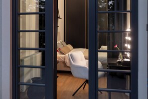Ein Zimmer mit einem Bett, einem Sessel, einem Schminktisch mit Beleuchtung und Blick durch eine Glastür.