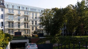 Ein mehrgeschossiges Gebäude mit Parkhaus-Einfahrt, einem weißen Auto, das einfährt, und einem gepflegten Garten.