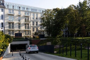 Ein mehrgeschossiges Gebäude mit Parkhaus-Einfahrt, einem weißen Auto, das einfährt, und einem gepflegten Garten.