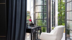Ein Zimmer mit großem Fenster, einem Schreibtisch mit Blumenvase und einem Sessel.