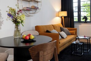 Ein modernes Wohnzimmer mit rundem Tisch, einer Couch, einer Lampe und einem Bücherregal.
