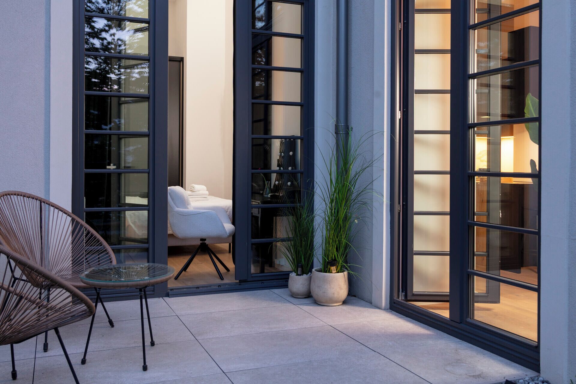 A modern outdoor seating area with a chair and a table, a potted plant, and a glass door leading to an interior space.