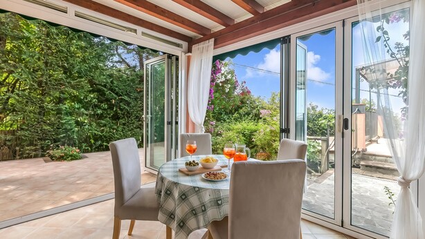 Een eethoek met een tafel gedekt voor twee personen, een schaal olijven, een bordje noten en twee glazen sinaasappelsap.