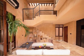 A spacious interior with a staircase leading to an upper level, a seating area with cushions, and a large plant. - Baia Villas Uluwatu (Pecatu)
