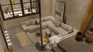 A modern living room with a sectional sofa, a small round table, a tall pillar, and a large window with a view of cacti. - Baia Villas Uluwatu (Pecatu)