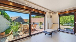 Moderni huone, jossa on suuri liukuovi, joka johtaa ulos terassille, jossa on ulkokalusteita ja ruukkukasveja.