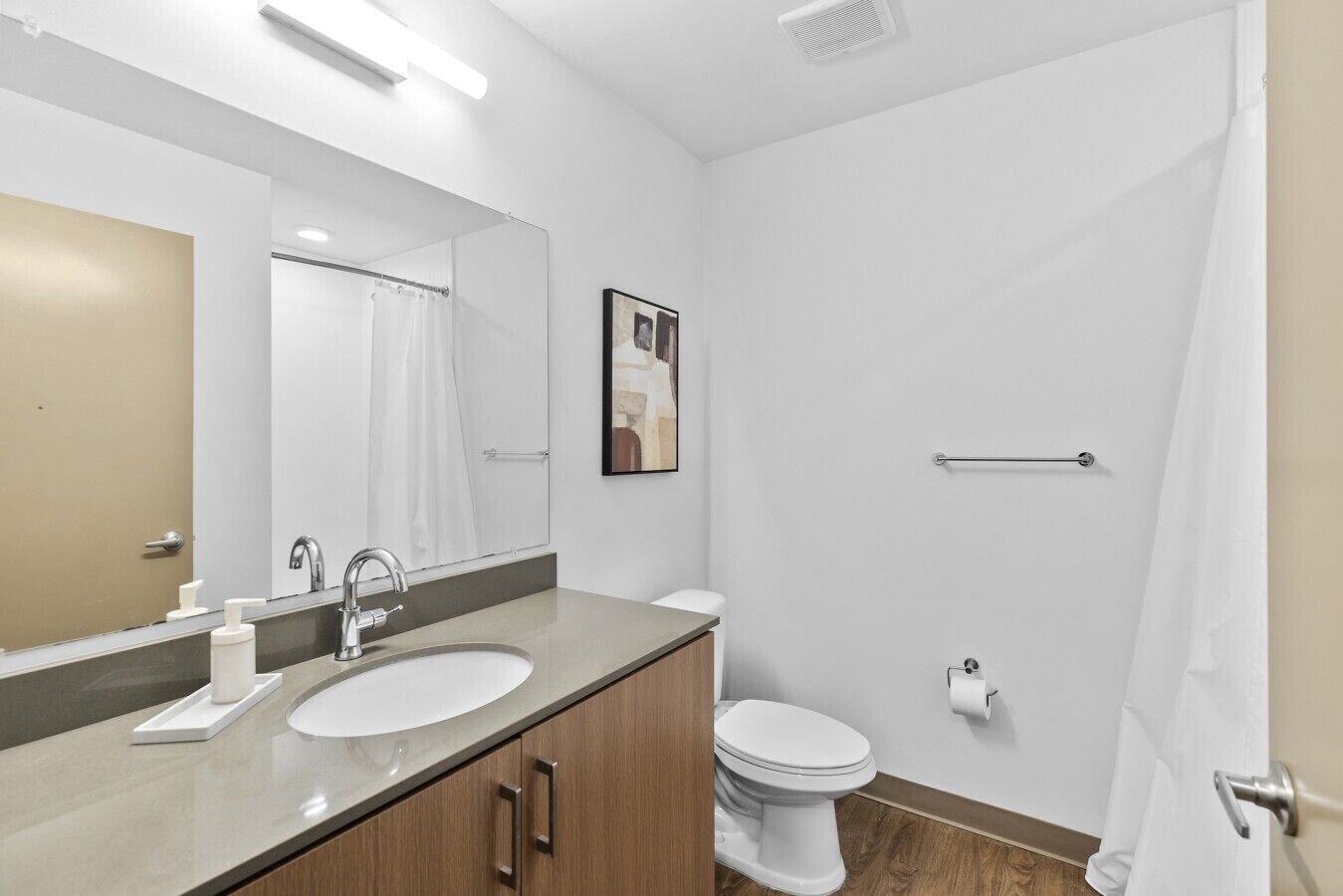 Une salle de bain moderne avec un double lavabo, des toilettes, un rideau de douche, un porte-serviettes et un tableau encadré au mur.