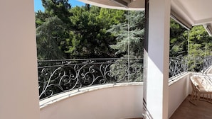 Un balcon doté d’un sol carrelé aux motifs courbes, d’une rambarde en métal ornée de motifs complexes, et offrant une vue sur les arbres et la verdure.