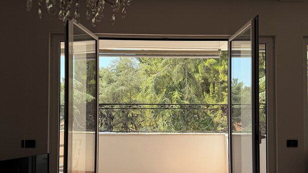 Une pièce dotée d’une grande porte-fenêtre coulissante donnant sur un balcon extérieur avec vue sur les arbres.