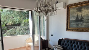 Un salon avec une porte vitrée donnant sur un balcon, un lustre, un canapé et un tableau accroché au mur.