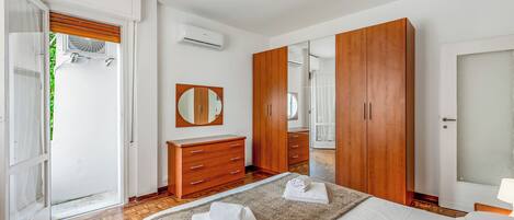 A bedroom with a bed, wooden wardrobe, a mirror, and a door leading to a balcony.