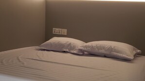 Una cama con ropa de cama blanca, un cabecero con iluminación integrada y un enchufe en la pared.