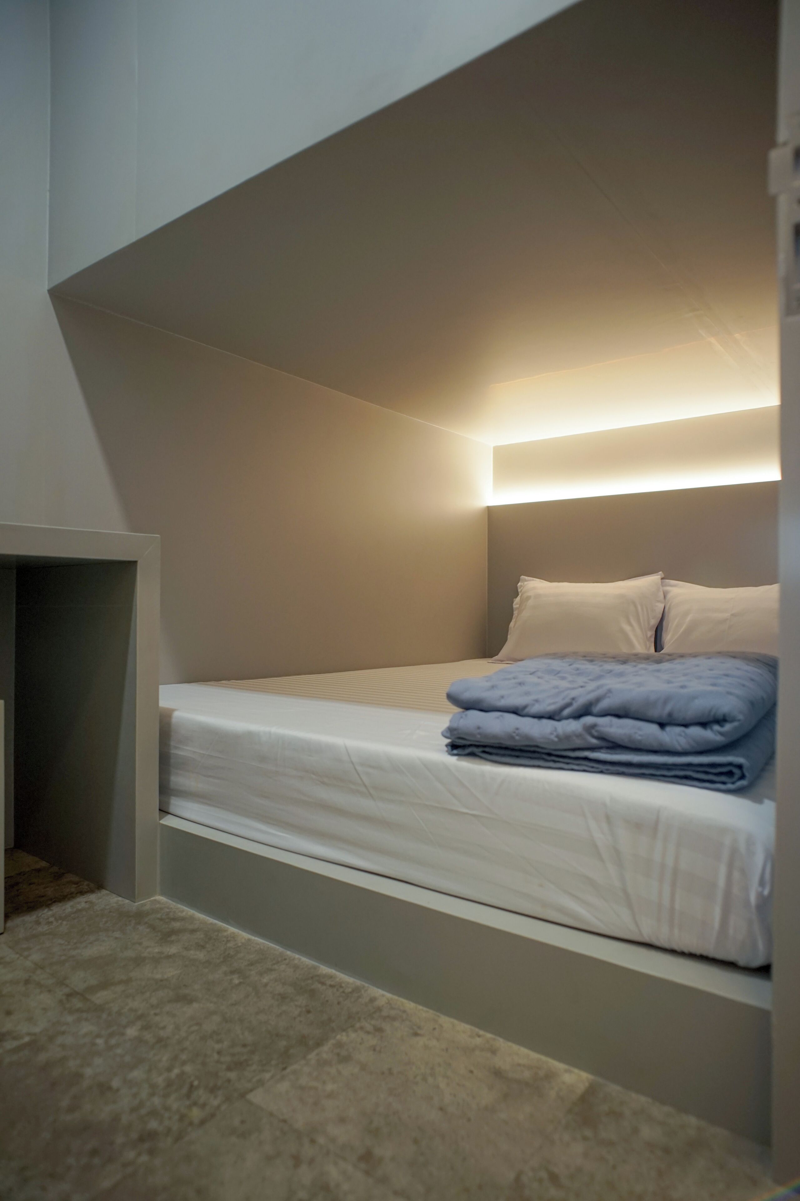 Ein kleines Zimmer mit einem Einzelbett, schräger Decke und einer eingebauten Sitzbank am Fußende.