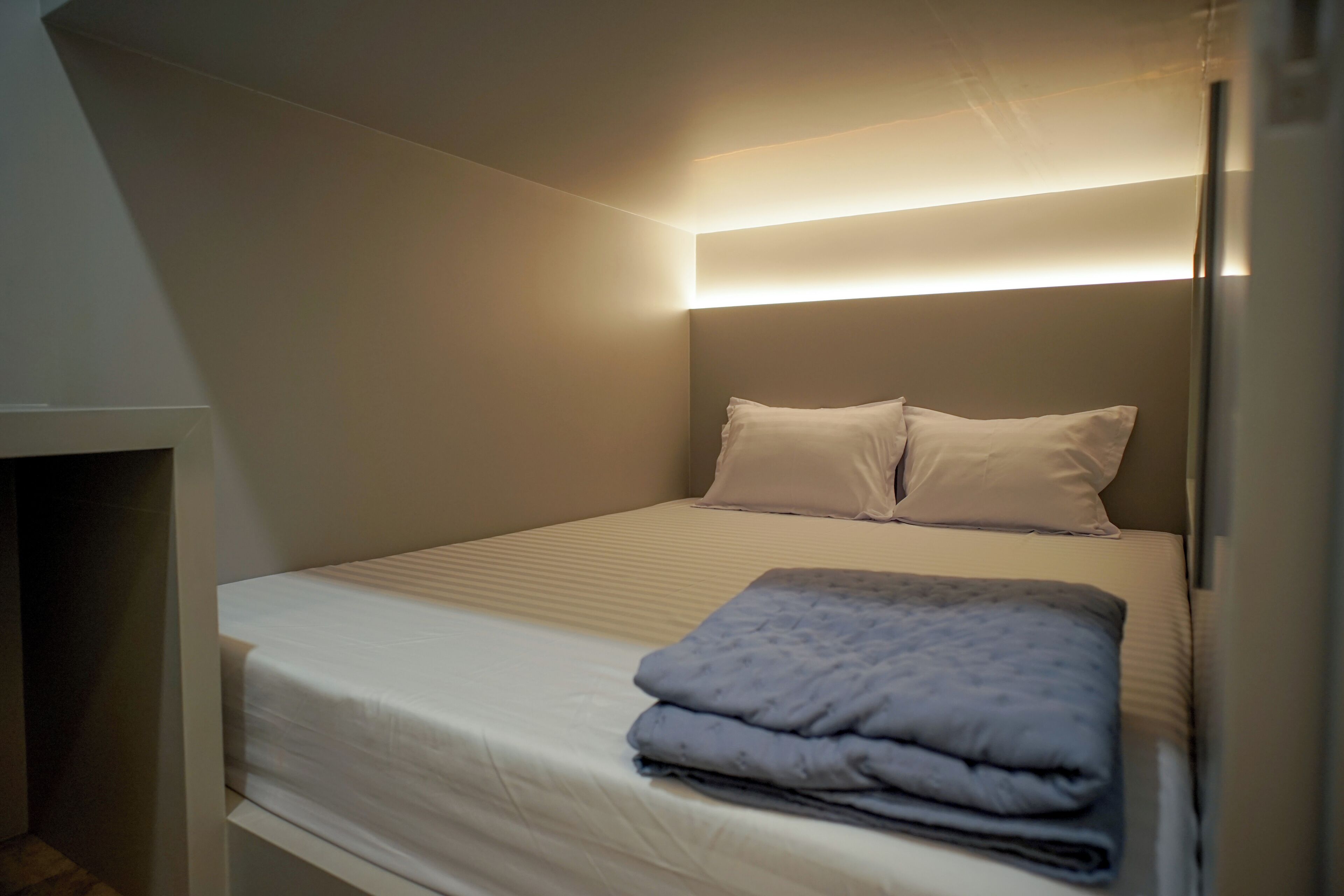 A single bed with a headboard, a bedside table, and a blanket.