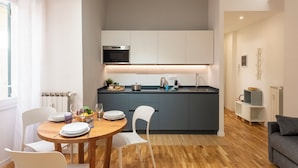 Une cuisine moderne avec des meubles blancs, un four encastré et un îlot central doté d’un évier.