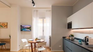 Une cuisine moderne dotée d’un four encastré, un coin repas avec une table en bois et des chaises blanches, et une vue sur un paysage montagneux par la fenêtre.