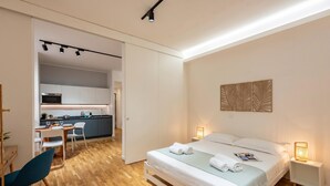 Une chambre d’hôtel moderne équipée d’un lit, de lampes de chevet, d’un bureau et offrant une vue sur la cuisine.
