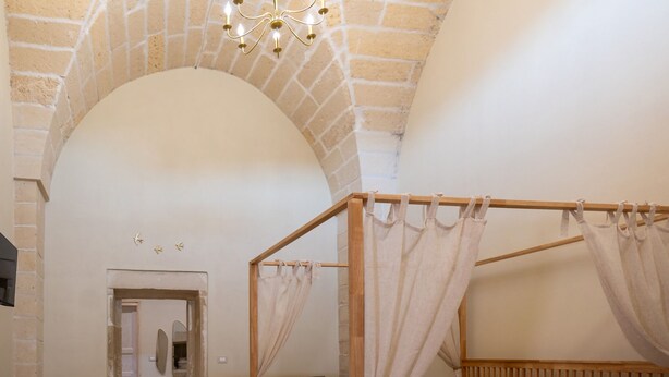 Een kamer met een hemelbed, een stenen boog, een houten plafond en een kroonluchter.