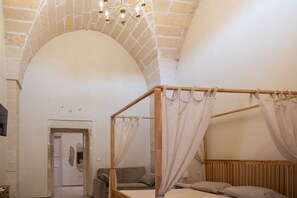 Een kamer met een hemelbed, een stenen boog, een houten plafond en een kroonluchter.