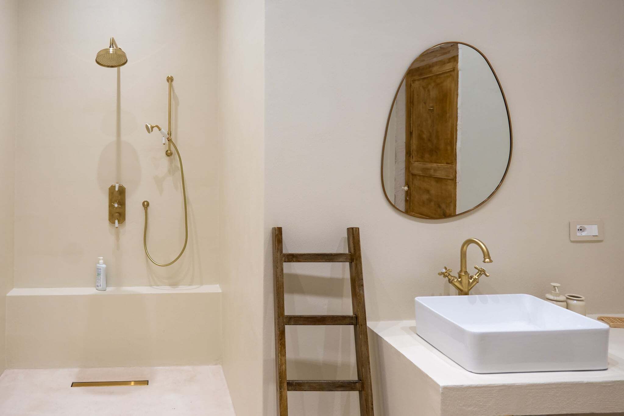 A bathroom with a shower, a sink, a mirror, and a wooden ladder.