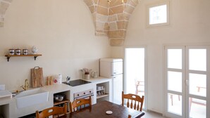 Een keuken met een stenen plafond, een inbouwfornuis, een gootsteen en een eettafel met stoelen.