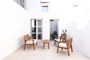 Una piccola area esterna recintata, con mobili in legno e un tavolo, una porta che dà su uno spazio interno e una finestra.