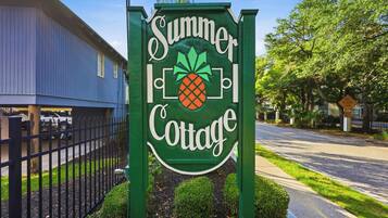 A sign for 'Summer Cottage' with a pineapple logo, surrounded by a fence and greenery.