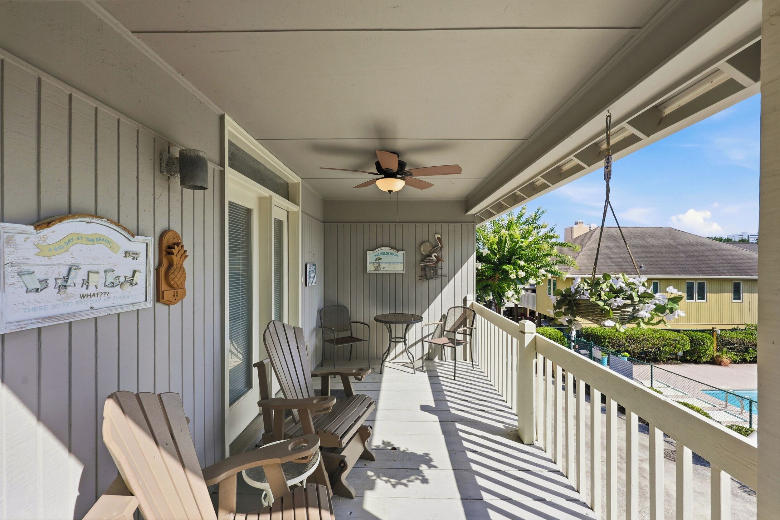 A covered porch with Adirondack chairs, a small table, and a ceiling fan.