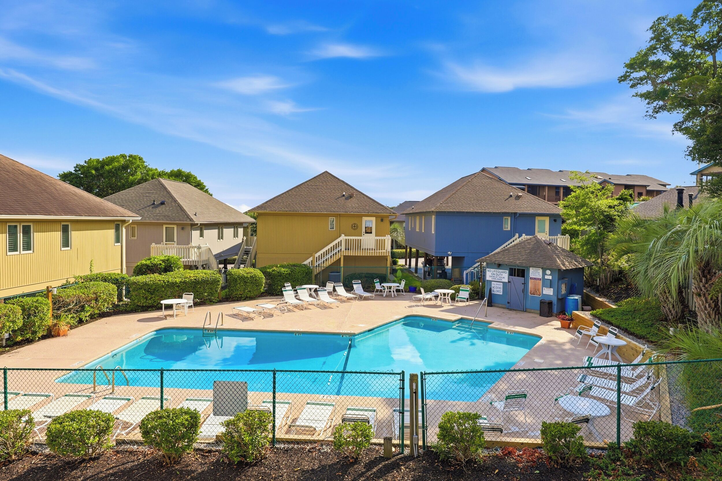 A residential-style hotel with a swimming pool, lounge chairs, and a fenced deck area.