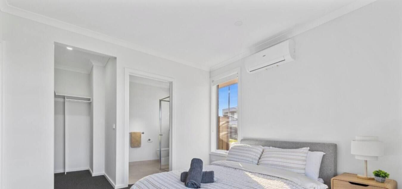 A bedroom with a bed, a nightstand, a window, and a door leading to a bathroom.