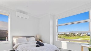 A bedroom with a bed, a nightstand, a lamp, and a window with a view of a residential area. - Spacious Modern Retreat in Officer | Perfect for Families (Officer)
