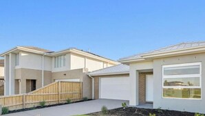 A residential building with a garage, a front yard with a wooden fence, and a clear sky. - Spacious Modern Retreat in Officer | Perfect for Families (Officer)