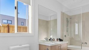 A modern bathroom with a toilet, vanity, mirror, and shower. - Spacious Modern Retreat in Officer | Perfect for Families (Officer)