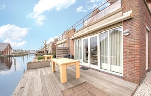 Ein Ufergrundstück mit Holzterrasse, Tisch und Glastür zum Balkon.