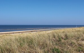Ein Strand mit Menschen, die am Ufer entlanggehen, einem klaren Himmel und Dünen im Vordergrund.