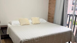 Una camera da letto con un letto, una finestra con tende e vista sugli edifici.