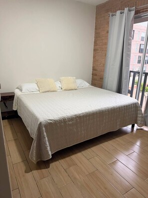 Ein Schlafzimmer mit Bett, einem Fenster mit Vorhängen und Blick auf Gebäude.