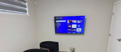 Un soggiorno moderno con una TV a schermo piatto montata a parete, mobili neri e una piccola pianta su un tavolino.