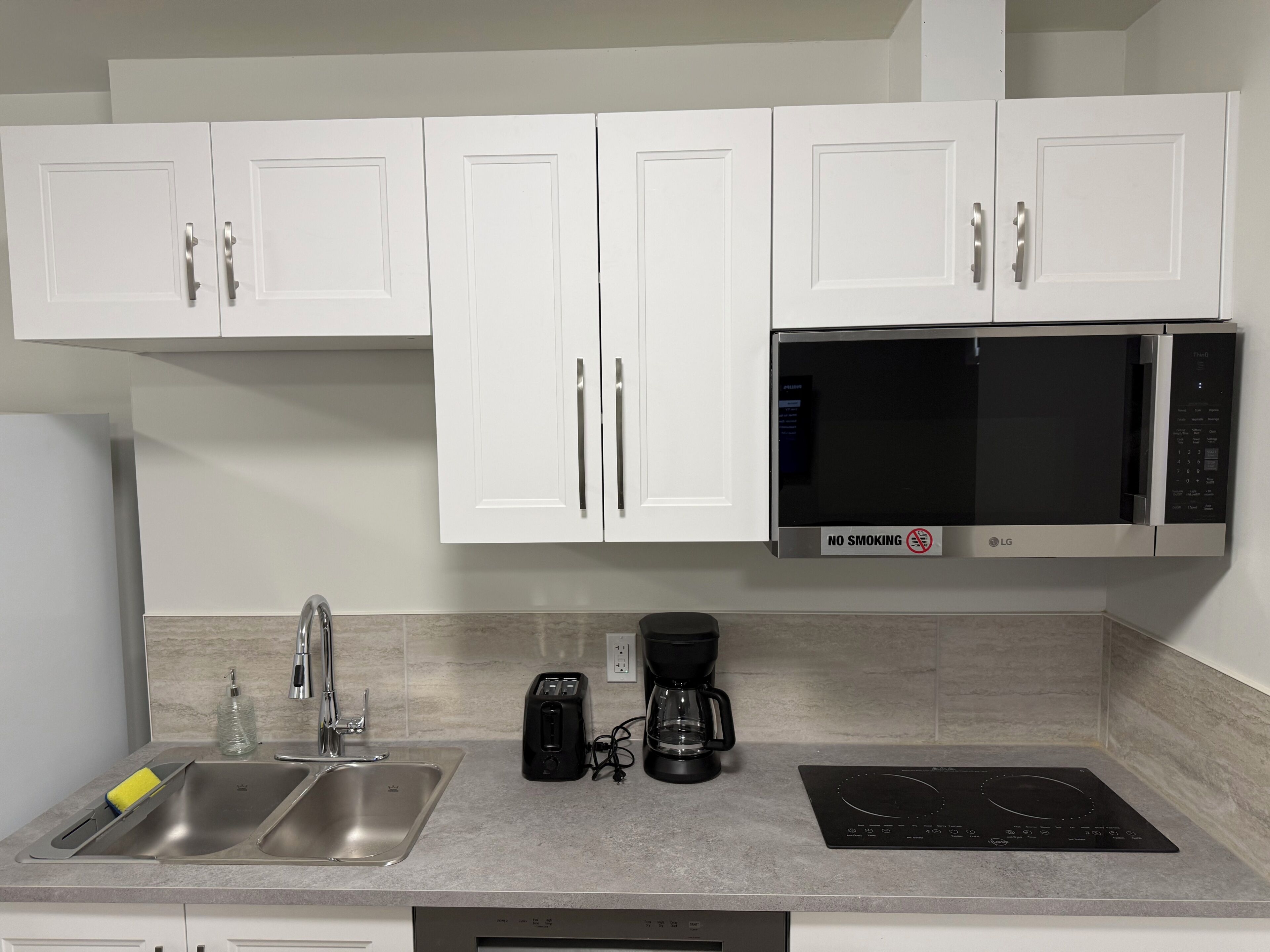 A modern kitchen with white cabinets, a stainless steel sink, a black microwave, a toaster, a coffee maker, and an induction cooktop.