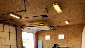 A spacious indoor area with a concrete floor, wooden walls, a large garage door, and several chairs.