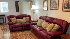 A living room with two red leather sofas, a wooden floor, a ceiling fan, and framed pictures on the wall.