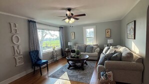 Un salon avec un ventilateur de plafond, un canapé, un fauteuil, une table basse et un tapis.