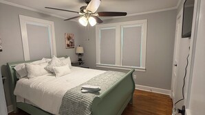 Une chambre à coucher avec un lit, un ventilateur de plafond, une fenêtre et une table de chevet.